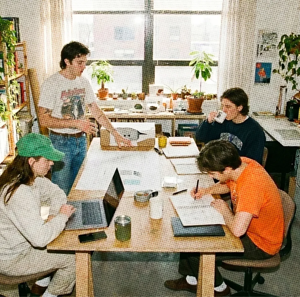 A product team collaborating around a table with laptops in a bright, plant-filled studio