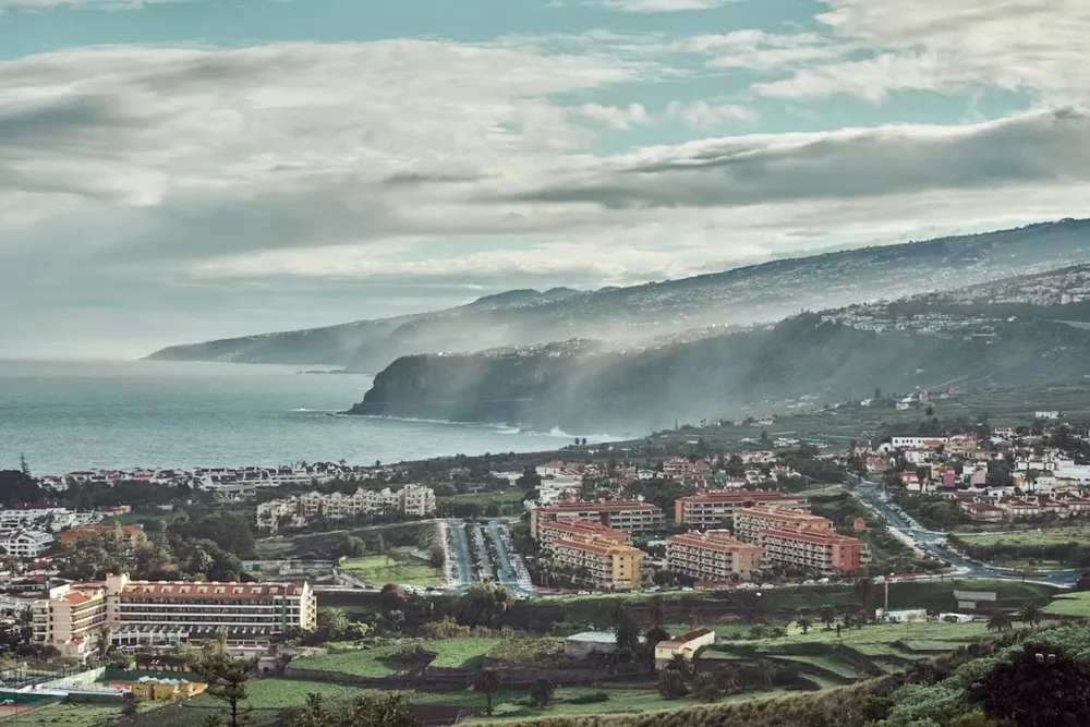 An ariel view of some hotel complexes and a sloping misty coastline in Tenerife
